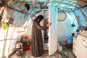 صبریه سرمیلی، ۵۸ ساله، دارای ۷ فرزند است. او روزها با دف زدن برای نوههایش، به آنها روحیه میدهد. همسر صبریه جانباز ۲۵ درصد است. آنها به همراه هم محوطه ورودی به چادر را با استفاده از نی به عنوان آشپزخانه ساختهاند.